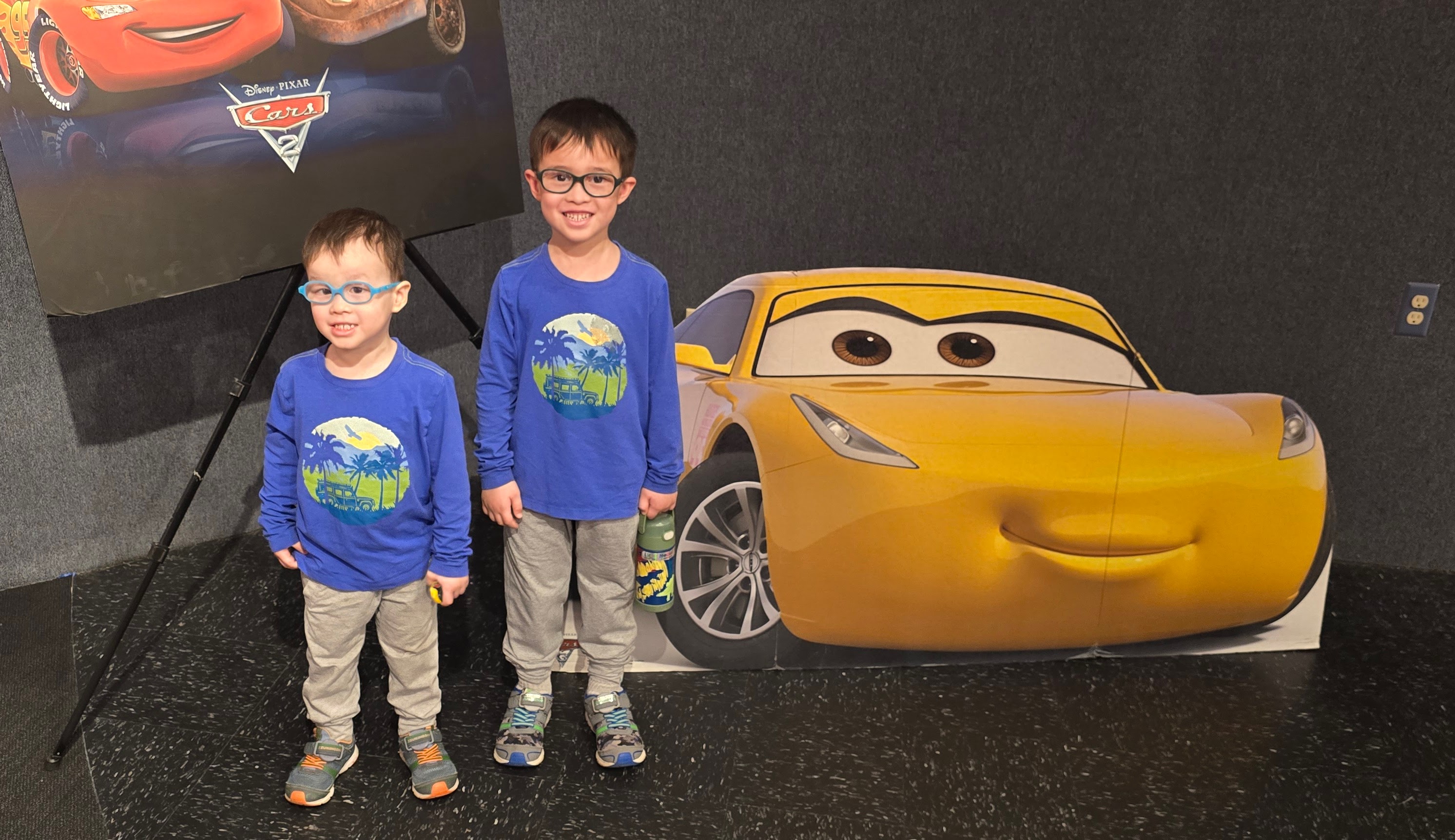 Two children beside a yellow Pixar Cars character display at an automobile museum
